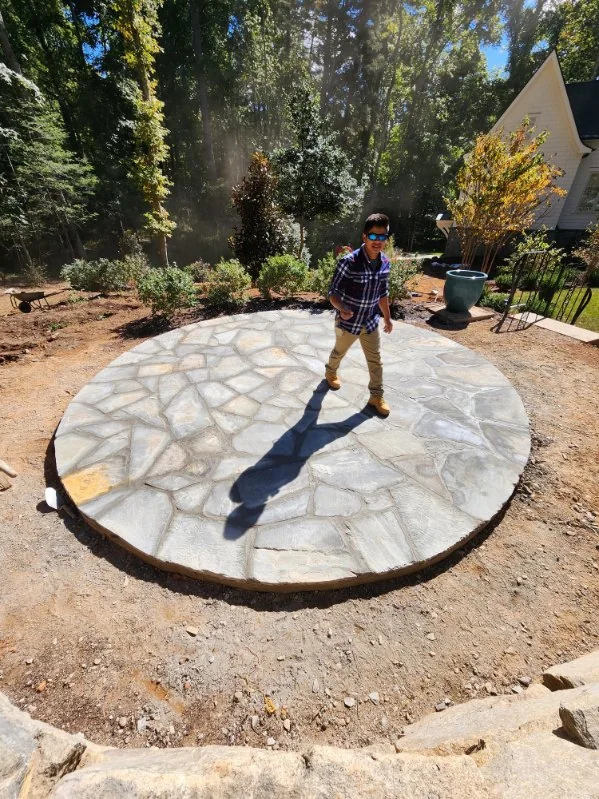 A round flagstone patio being fitted at the tree line